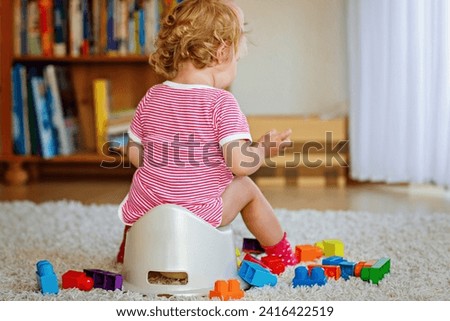 Closeup of cute little 12 months old toddler baby girl child sitting on potty. Kid playing with doll toy. Toilet training concept. Baby learning, development steps