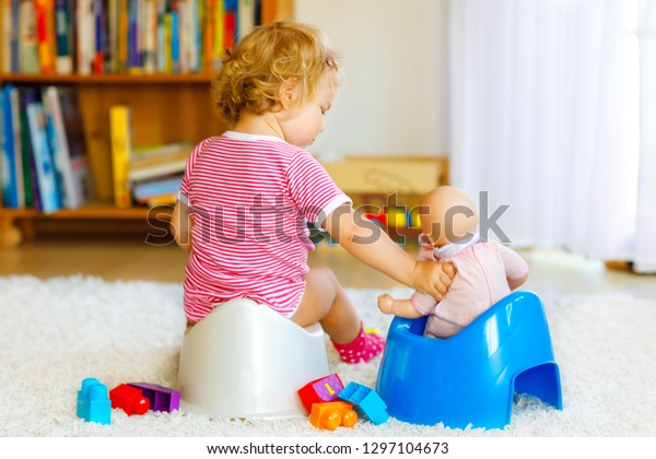 Closeup of cute little 12\
months old toddler baby girl child sitting on potty. Kid playing\
with doll toy. Toilet training concept. Baby learning, development\
steps