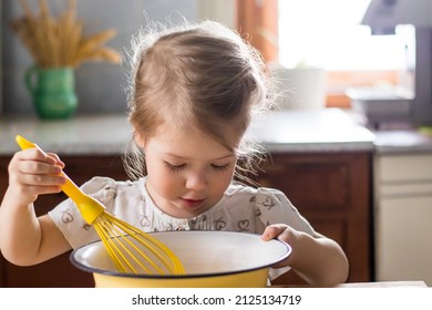 Close-up of a cute little girl kneading dough on a wooden table. A child helping his mother to cook a pie kneading the dough in the light kitchen with natural light coming through a window.