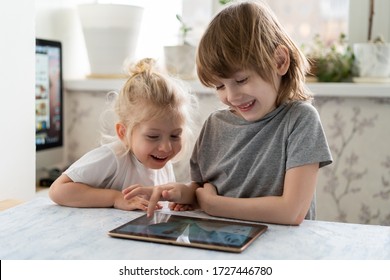 Close-up of a cute little sister and brother sitting close to each other, smiling while watching something on a tablet device or playing a game on it. Indoors - Powered by Shutterstock