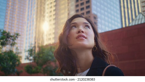 Closeup Cute Woman Looking Back On High Building Going City Street. Portrait Of Attractive Asian Girl On Sunlight. Beautiful Girl Face Watching Up On Cityscape. Pretty Lady Walking Alone On Megapolis.