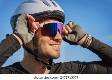 Close-up of a cyclist adjusting his white helmet and reflective sunglasses, smiling brightly against a clear blue sky.

 - Powered by Shutterstock