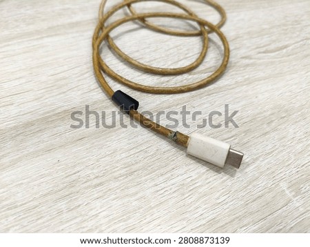 ​Vertical close-up of a damaged and dirty USB Type-C charging cable with green corrosion on a wooden desk. Concept of electronic waste, broken technology, or fire hazard from worn-out wire.