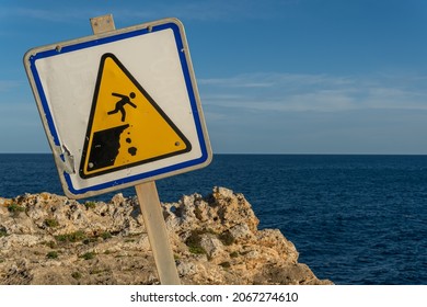 Close-up of a danger sign for people falling down a ravine, crooked. In the background the Mediterranean Sea on the island of Mallorca at sunset - Shutterstock ID 2067274610