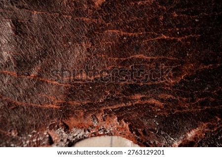 Close-up of dark brown leather texture with reddish veins and worn edges, showing grain and stitching area