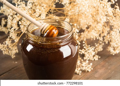 Closeup Of Dark Honey With Spoon With Flowers On Background