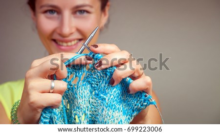 Close-up of a dark-haired beautiful woman smiling and knitting with knitting needles from a natural woolen thread a white and blue sweater, a woman shows how to knit correctly