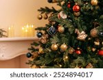 A close-up of a decorated Christmas tree with vintage glass toys. Stylish rich interior with fireplace and lighted candles. New year decorations. Copy space.