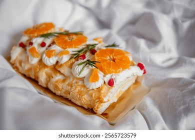 A close-up of a decorative pavlova roll topped with fresh orange slices, pomegranate seeds, and whipped cream, presented on a white background. Festive sweet dessert - Powered by Shutterstock