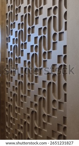 A close-up of a decorative wall panel with a repeating, modern geometric pattern of interlocking curves and squares.