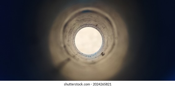 Close-up deep endless round large and long concrete pipe hole with blurry black foreground and white background with copy space. Bore well, drainage, pipeline, mining and factory sewage concept.