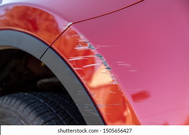 Closeup of deep scratches in red paint of car bumper