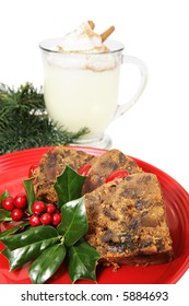 Closeup Of Delicious Christmas Fruitcake Garnished With Holly And A Mug Of Eggnog In The Background.  Isolated On White.