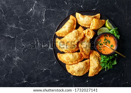 close-up of delicious deep fried Buffalo Chicken Empanadas with Low Calorie Dip on a black platter on a concrete table, horizontal view from above, flat lay, free space