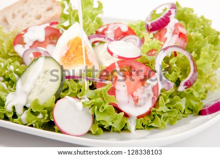 Closeup of a delicious mixed green salad with egg, onion, tomato and cucumber drizzled with a tangy salad dressing for a healthy meal