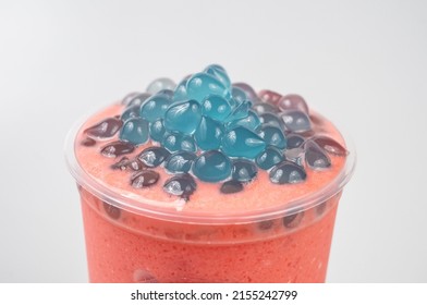 A Closeup Of A Delicious Pink Bubble Tea With Small Blue Boba On Top On A White Background