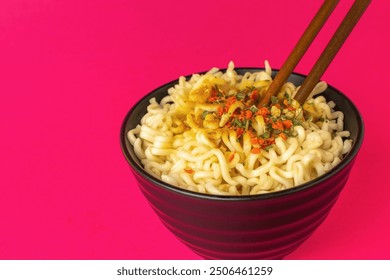 Close-up of Delicious Spicy Noodles in Black Bowl with Chopsticks on Vibrant Pink Background - Powered by Shutterstock