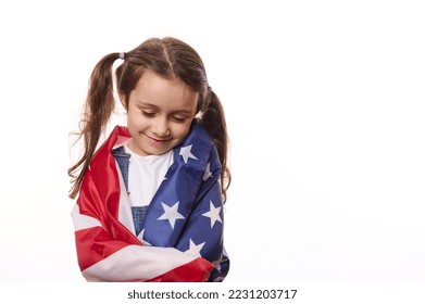 Close-up of delightful little girl with two cute ponytails, hugs herself, covered on United States of America flag, on independence day, isolated over white background, with space for your advertising - Shutterstock ID 2231203717