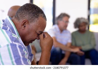 Close-up of depressed caucasian senior man with head in hand sitting with multiracial friends. Unaltered, sad, group therapy, emotional stress, together, support, assisted living, retirement home. - Powered by Shutterstock