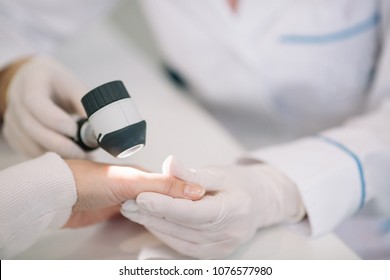Closeup of dermatologist examining mole on hand of female patient in clinic