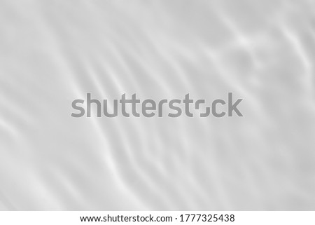 Closeup of desaturated transparent clear calm water surface texture with splashes and bubbles. Trendy abstract nature background. White-grey water waves in sunlight.