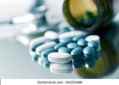 closeup of the desk of a doctors office with a bottle with pills in the foreground and a stethoscope in the background
