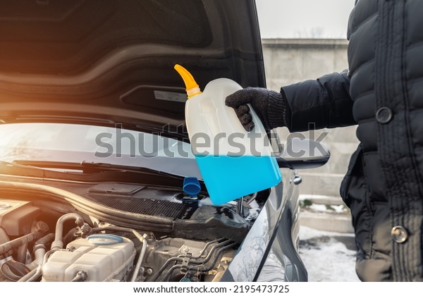 Close-up detail of driver or mechanic hand in\
gloves pouring blue antifreeze liquid for winter car windshield\
screen washing with bootle watering can. Car seasonal service and\
maintenance concept