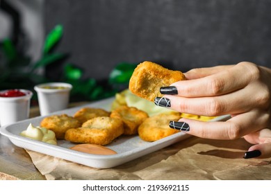 Close-up Detail Of A Latin Girl's Hand Holding A Nugget, A Plate With Chicken Nuggets With Potatoes And Mozzarella Cheese, Served On A Wooden Tray, With Two Small Glasses With Sauce.