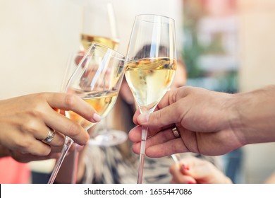 Close-up Detail Of Men And Woman Hands Clinking Glasses Of White Champagne Or Prosecco At Party Or Celebration Event Outdoors. People Having Fun Enjoy Drink Alcohol Toasting Cheers At Cafe Restaurant