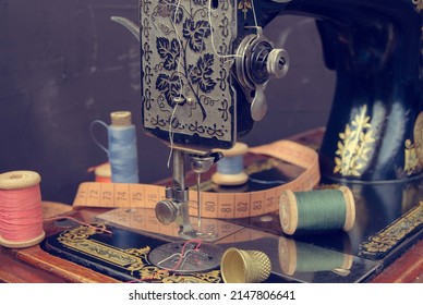 Close-up detail of an old sewing machine,coils of multicolored thread,thimble, sewing tape Concept: sewing clothes with your own hands, clothing history, vintage sewing accessories. Retro tinting