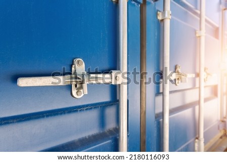 Close-up detail view of big blue metal freight cargo container door handle closed with padlock lock. Storage warehouse safety. Commercial shipping port. Export and import goods customs clearance