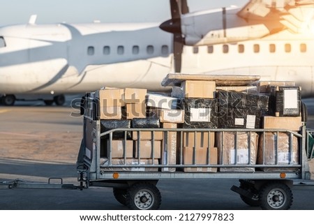 Close-up detail view of cargo cart trolley full with commercial parcels against turboprop cargo plane. Air mail shipping and logistics. Import export operations. Commercial charter flight service