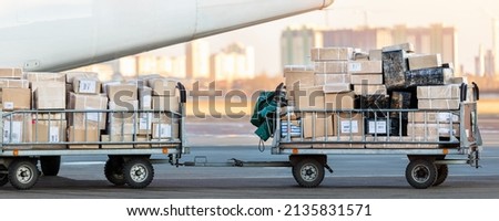 Close-up detail view of cargo cart trolley full with commercial parcels against turboprop cargo plane. Air mail shipping and logistics. Import export operations. Commercial charter flight service