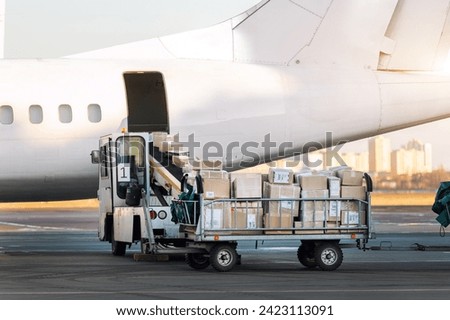 Close-up detail view of cargo cart trolley full with commercial parcels against turboprop cargo plane. Air mail shipping and logistics. Import export operations. Commercial charter flight service