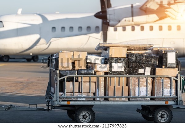 Close-up detail view of cargo cart trolley full\
with commercial parcels against turboprop cargo plane. Air mail\
shipping and logistics. Import export operations. Commercial\
charter flight service