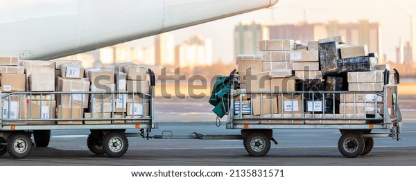 Close-up detail view of cargo cart trolley full\
with commercial parcels against turboprop cargo plane. Air mail\
shipping and logistics. Import export operations. Commercial\
charter flight service