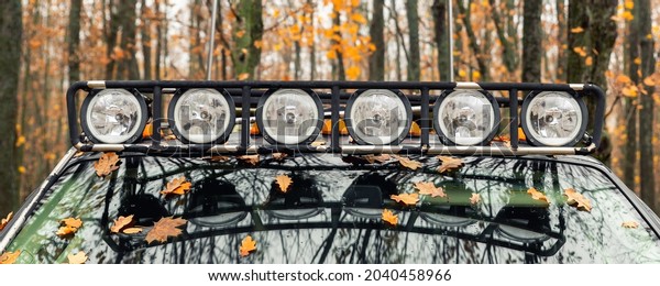 Close-up detail view of custom made roof rack bar\
with extra headlight mounted on roof of heavy duty pick up suv car\
against foggy autumn forest. Fallen leaves vehicle windshield. Fall\
weather drive