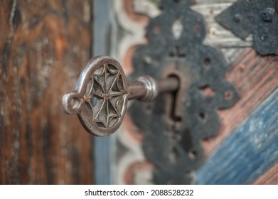 Closeup detail view of old massive metal key in a large huge church wooden ancient door. Secret mystery entrance. Traditional gothic grunge vintage style. Medieval security and safety