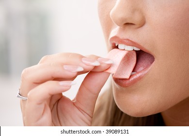 Closeup Detail Of Woman Putting Pink Chewing Gum Into Her Mouth.