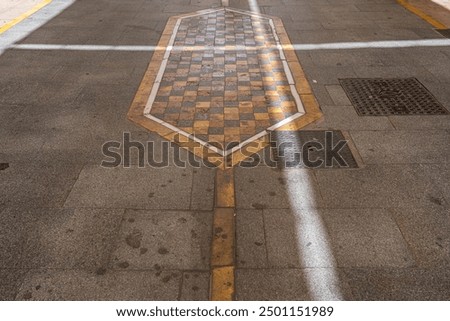 A close-up of detailed tilework featuring warm tones and a central drain grate on a street in Ronda, Spain. Perfect for themes of urban design, architectural details, and street photography