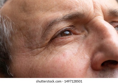 A closeup and detailed view on the brown eye of an elderly male. Wrinkles and crow's feet are seen around the eye and forehead of older man deep in thoughts.