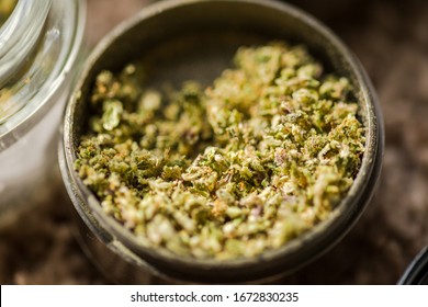 Close-up details of ground cannabis flower in a metal grinder. Fresh and high-quality green buds in steel grinder.
