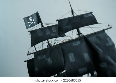 Close-up details of Pirate ship model Black made of plywood. Flag Jolly Roger Skull and bones in focus, partially blurred patched sails and ropes