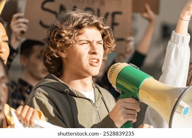 Close-up of a determined young man with curly hair using a megaphone during a demonstration. Image captures youth leadership, passion, and commitment in social activism - Powered by Shutterstock