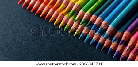 A close-up, diagonal arrangement of sharpened colored pencils showcasing a spectrum of vibrant colors on a dark, textured background.