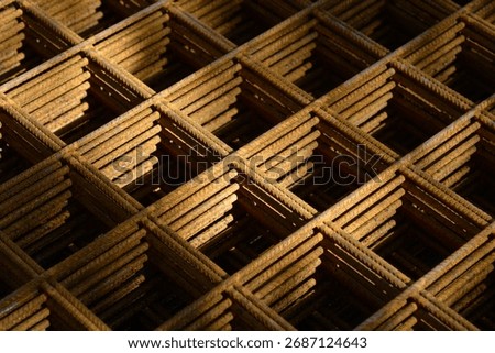  A close-up, diagonal view highlights the rusty, stacked layers of welded wire mesh (rebar grid) used for concrete reinforcement, creating a repeating geometric pattern with deep shadows