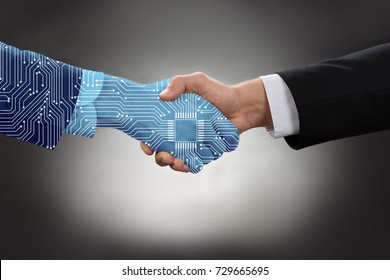 Close-up Of Digital Generated Human Hand And Business Man Shaking Hands Against Grey Background
