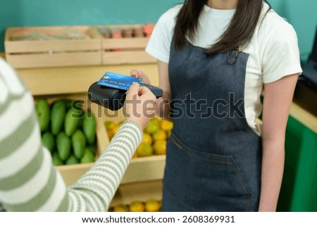 Closeup of digital payment process using contactless credit card in tropical fruit shop between Asian female customer and seller showing seamless technology in small business environment
