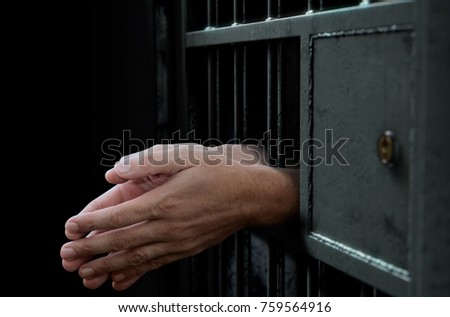 A closeup of a dimly lit prison holding cell door with arms reaching out in a praying position - 3D render