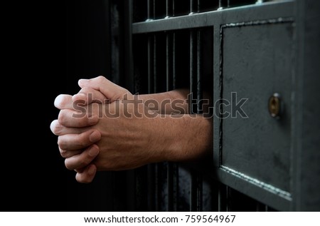 A closeup of a dimly lit prison holding cell door with arms reaching out in a clenched prayer position - 3D render